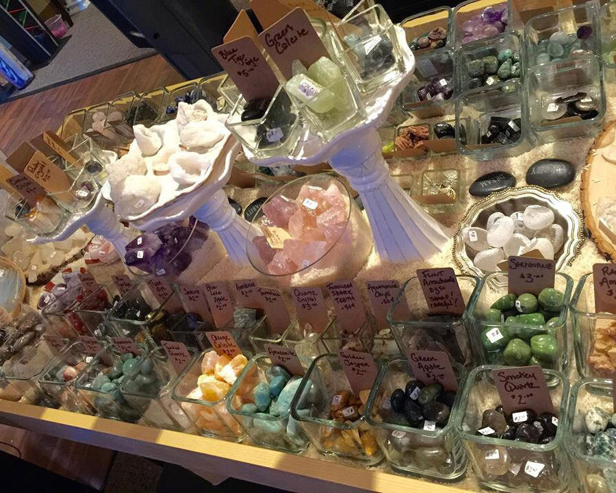 Display of various crystals and stones in glass containers with price tags.