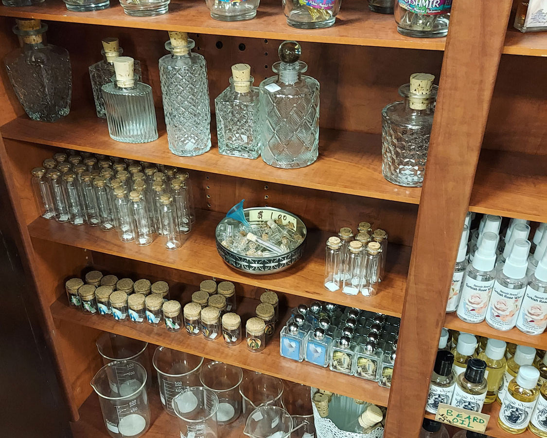 Wooden shelves with various bottles, perfume testers, holy water containers, beakers, sprays, beard oil, and more.