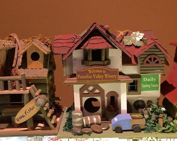 Collection of decorative birdhouses mimicking a winery, beach shack, cabin, and more with signs and decorated yards.