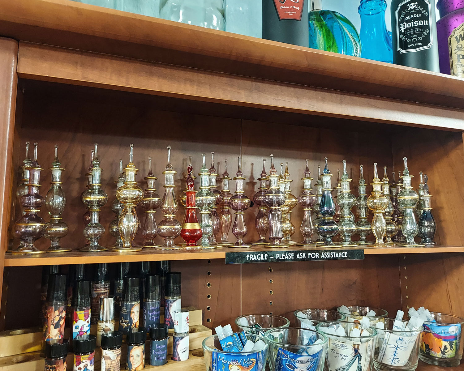 Shelves of fancy blown-glass perfume bottles in various colors and shapes above our standard oil perfume roller bottles.