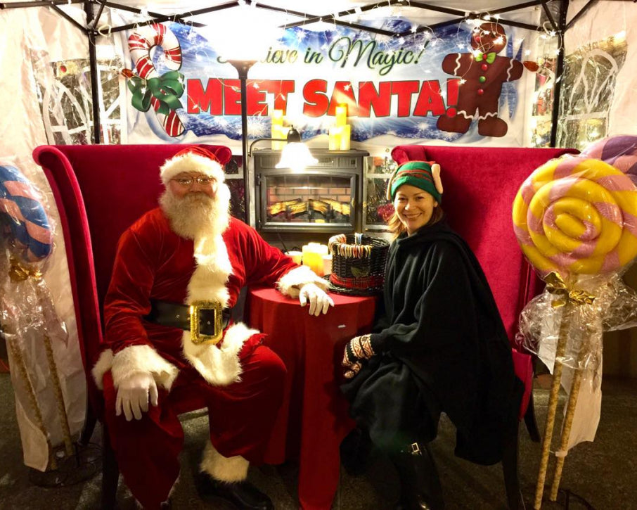 Person in Santa costume sitting with a person in a green hat and black coat at a 'Meet Santa' event at our shop.