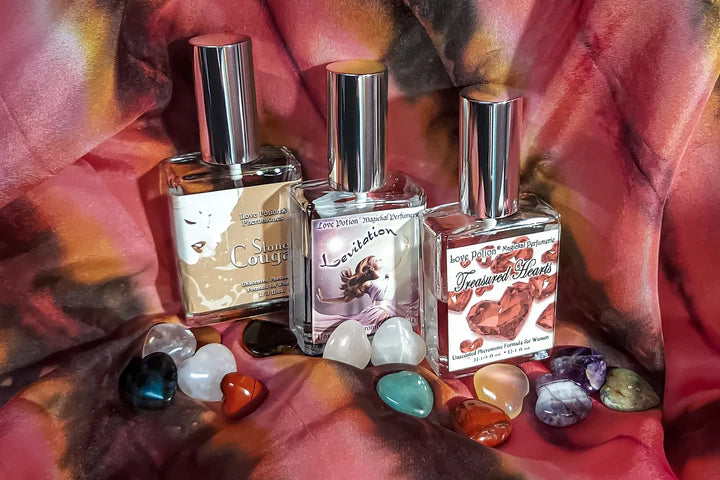 Three pheromone spray bottles with colorful labels on a tie-dye fabric background with heart-shaped crystals.