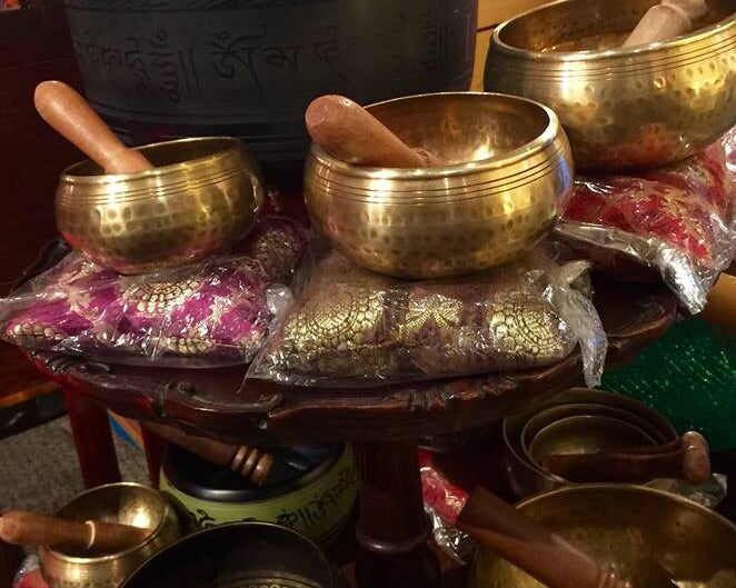 Collection of brass singing bowls on a table with wands and other mystical items in the background.