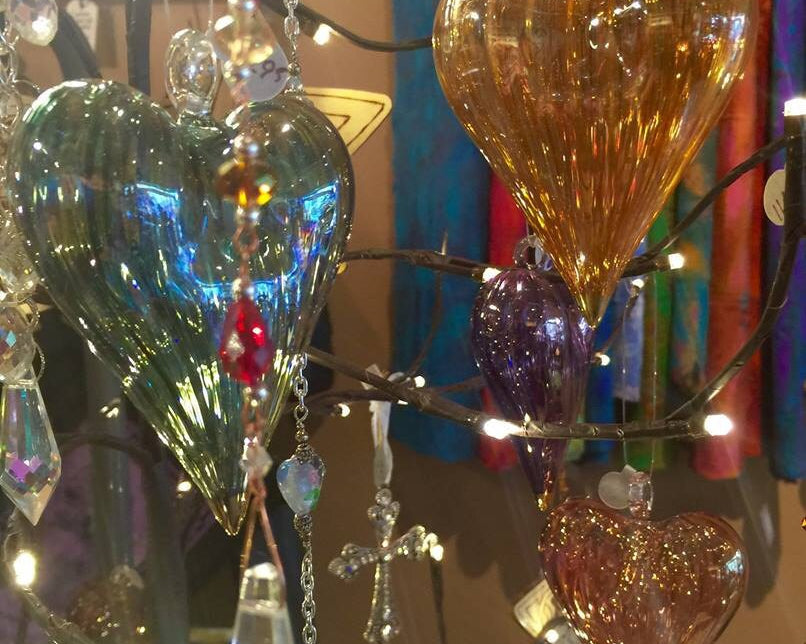 Colorful glass heart ornaments hanging on lighted branches with tie-dye tapestries hanging in the background.