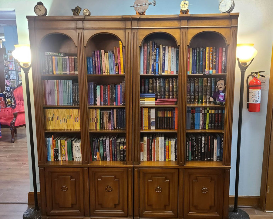 Wooden bookshelf filled with books in the library and snack bar area of the shop, with lamps and clocks.