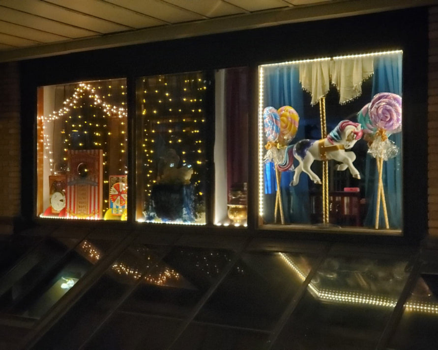 Decorative window display with carnival, carousel, and candy-themed decorations.