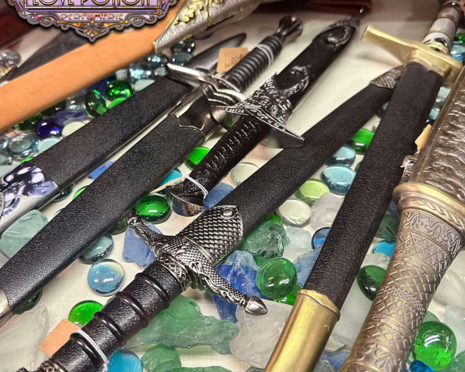 Seven daggers laid out in our dagger display case over blue and green glass pebbles.
