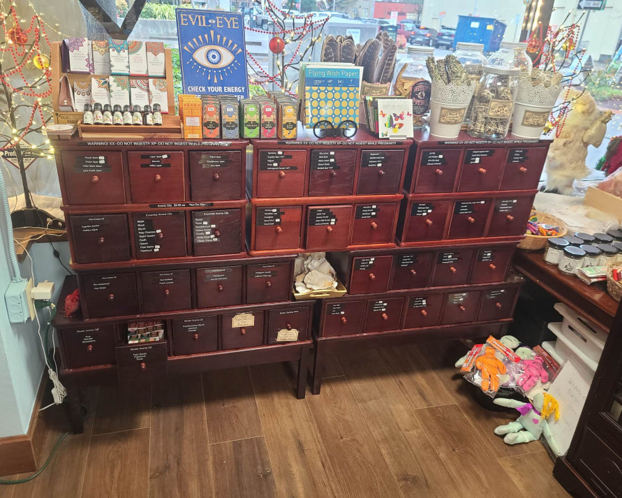 The image displays a cabinet filled with different spell ingredients. On top are feathers, sage, and lavender.