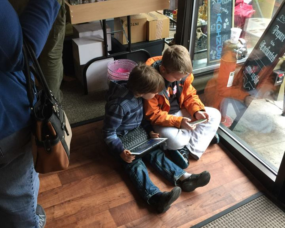 Two children in our store entertaining themselves with a laptop and smart phone on the floor while their parents shop.