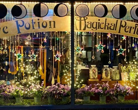 Magical Perfumerie window display with potion bottles, flowers, moon phases, and giant mushrooms.