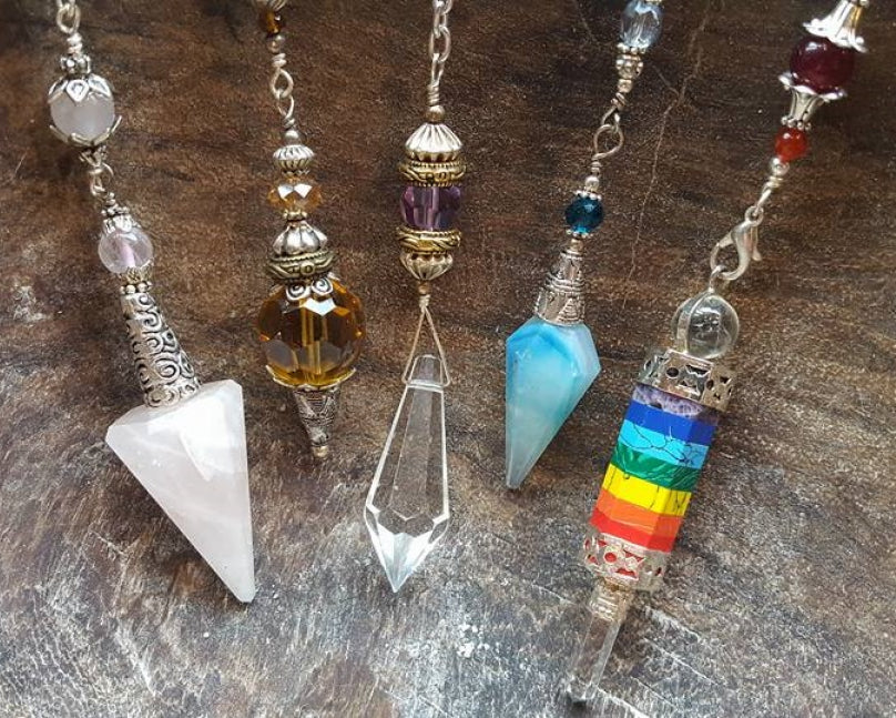 5 different types of crystal pendulums on display in front of a wooden background.