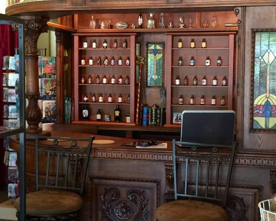 Wooden bar with stained glass panels and shelves filled with perfume bottles, surrounded by chairs.