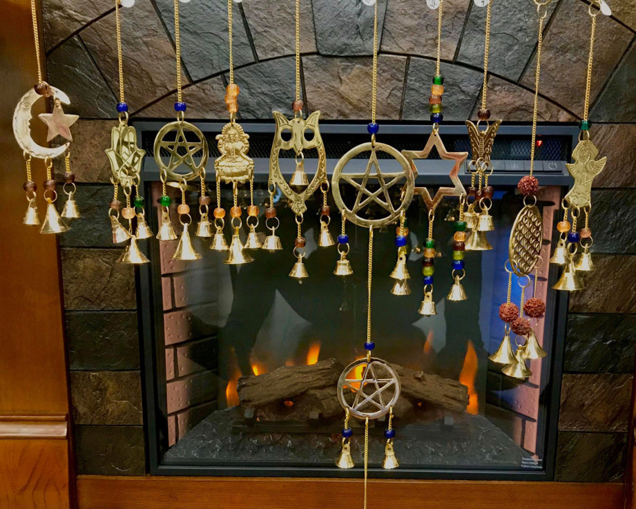Different varieties of metal wind chimes being shown in front of a fireplace with the fire going.