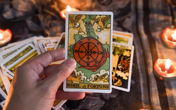 Hand holding a tarot card with candles and cards in the background.