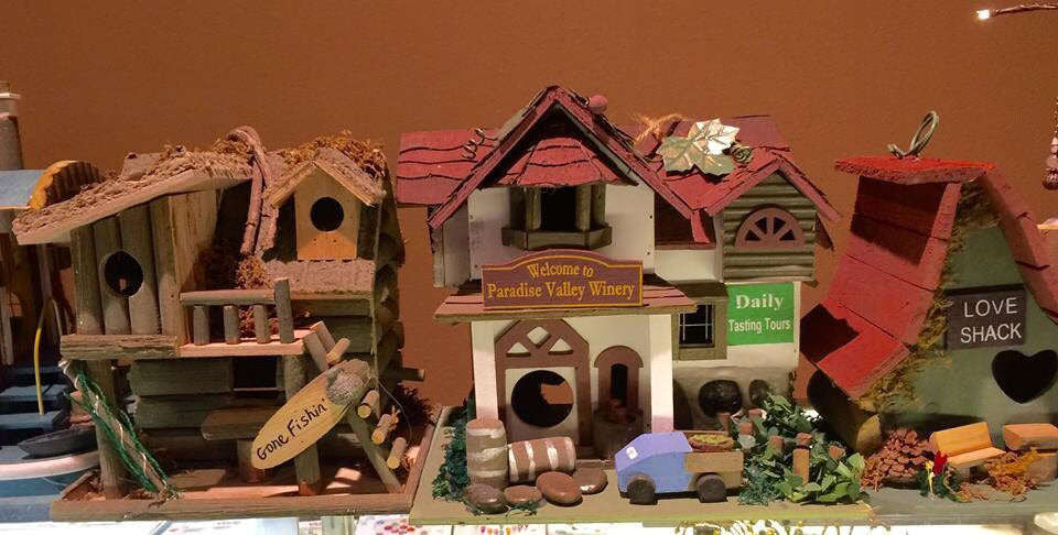 Collection of decorative birdhouses mimicking a winery, beach shack, cabin, and more with signs and decorated yards.