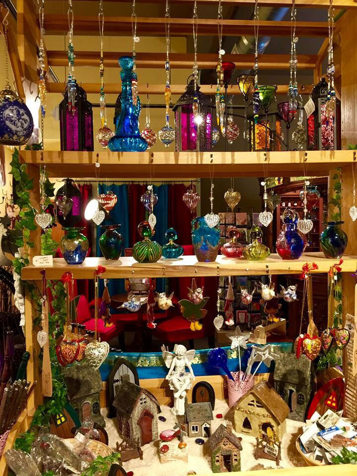 Display of various decorative items including hanging ornaments and fairy garden houses on a wooden shelf.