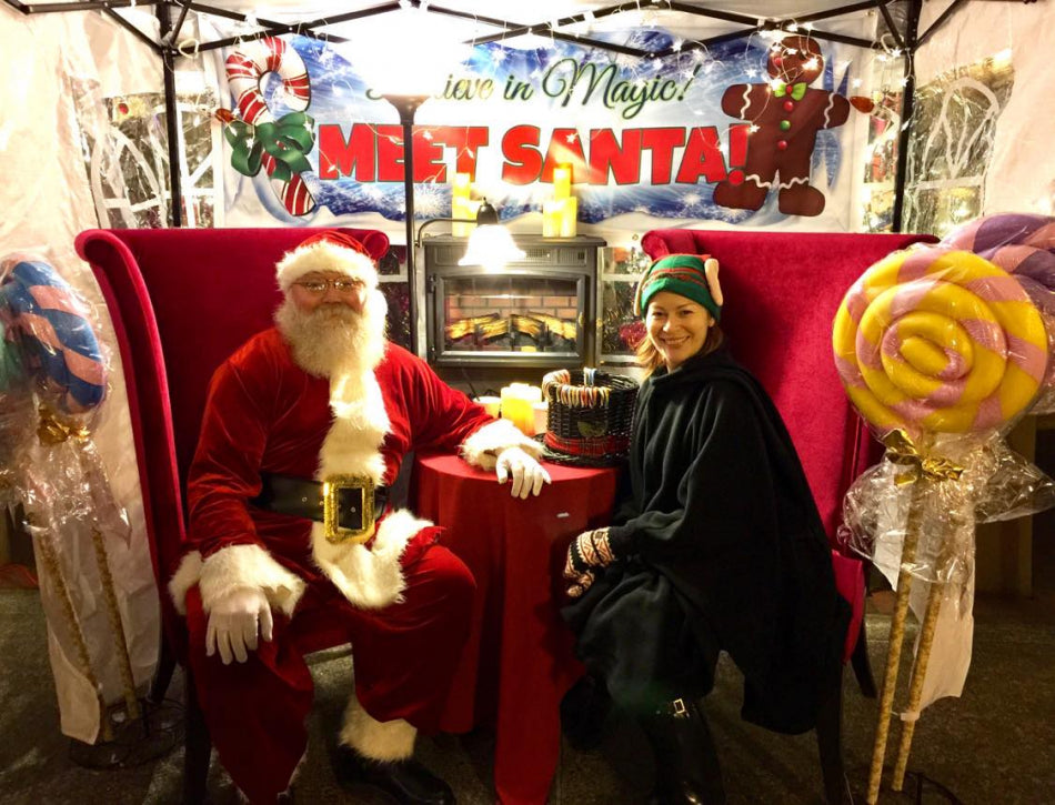 Person in Santa costume sitting with a person in a green hat and black coat at a 'Meet Santa' event at our shop.