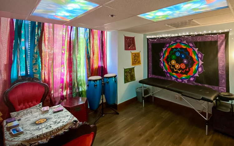 Rent-able Room of Requirement with a tarot table, massage table, a large tapestry on the wall, and colorful curtains.