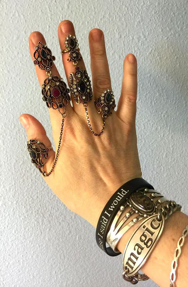 Hand wearing multiple ornate rings and bracelets against a plain background.