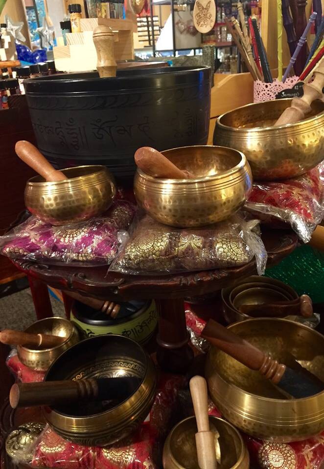 Collection of brass singing bowls on a table with wands and other mystical items in the background.