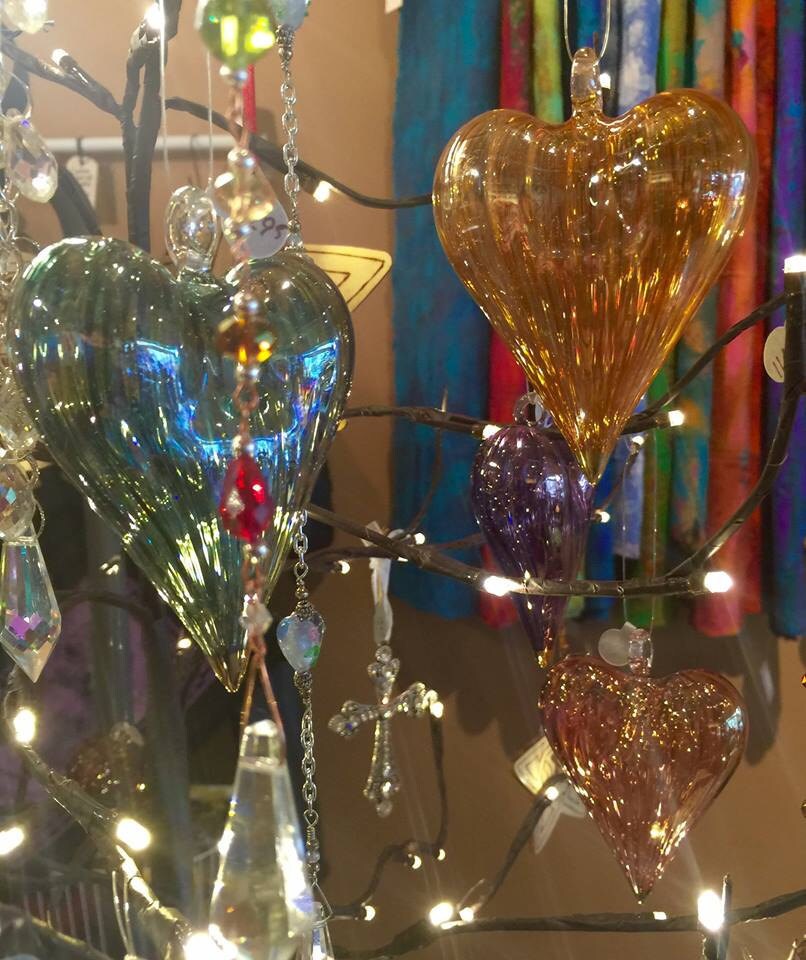 Colorful glass heart ornaments hanging on lighted branches with tie-dye tapestries hanging in the background.