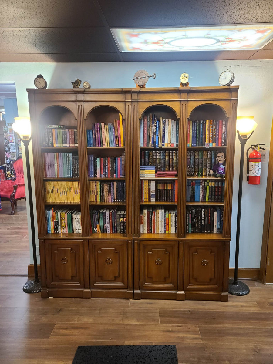 Wooden bookshelf filled with books in the library and snack bar area of the shop, with lamps and clocks.