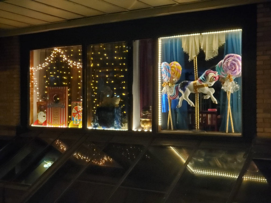 Decorative window display with carnival, carousel, and candy-themed decorations.