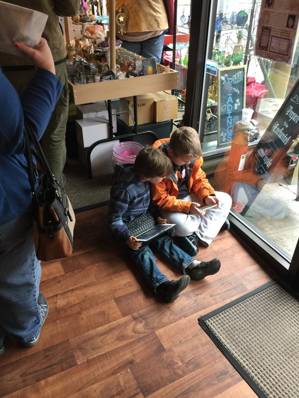 Two children in our store entertaining themselves with a laptop and smart phone on the floor while their parents shop.