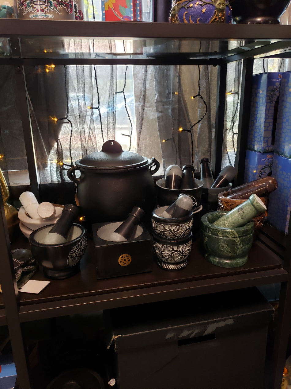 Many mortar and pestles on display. They are on a shelf with the sun shining through a window in the background.