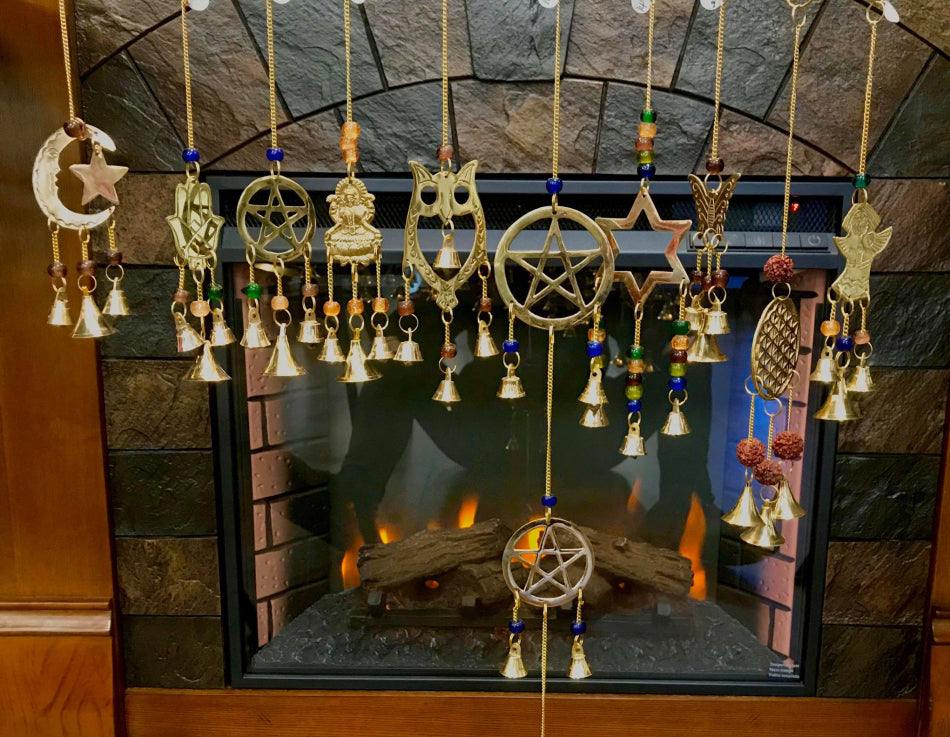 Different varieties of metal wind chimes being shown in front of a fireplace with the fire going.